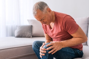 Older man sitting on couch grasping leg in pain