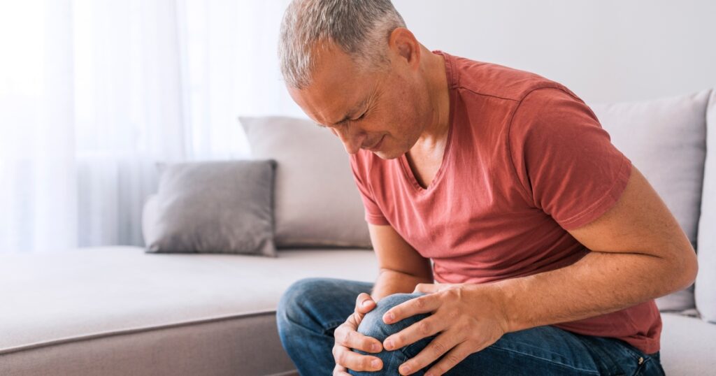 Older man sitting on couch grasping leg in pain